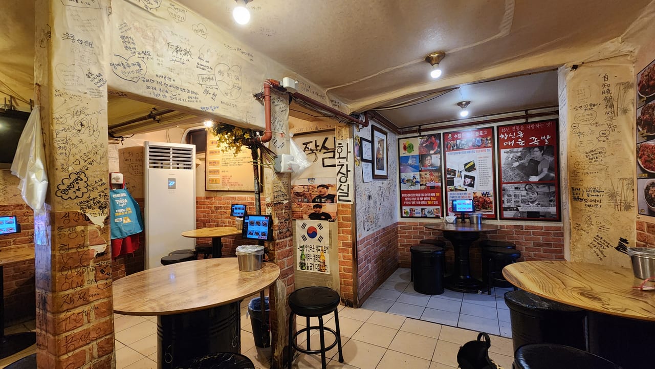 Compact interior of Changsin-dong Spicy Jokbal with round tables and signature-covered walls