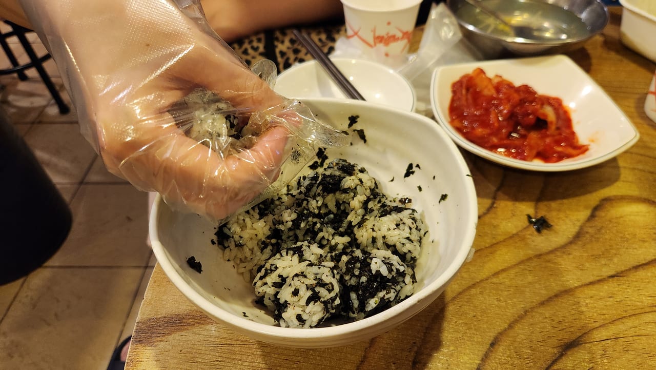 A gloved hand rolling seaweed rice into Korean jumeokbap balls