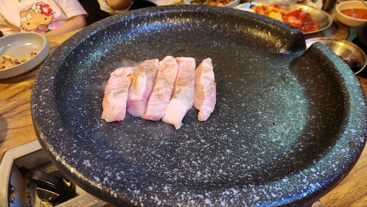 Thick slices of pale pink hangjeongsal cooking on a round barbecue pan