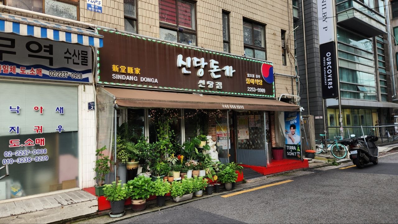 Sindang Donga exterior with many potted plants beneath the restaurant sign