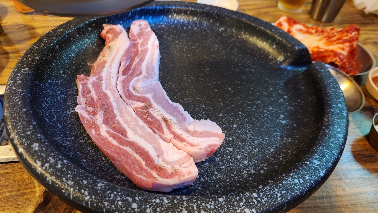 Thick raw strips of fresh samgyeopsal on the round barbecue pan